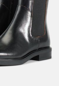 Botas de tobillo de cuero negro con paneles laterales elásticos, una parte superior lisa, costuras en marrón y un tacón bajo apilado.