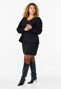 Blusa nera con texture, maniche lunghe a palloncino e scollatura a V, abbinata a una gonna nera aderente e stivali neri lucidi fino al ginocchio.