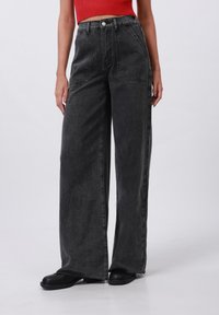 Pantalons en denim noir taille haute à jambes larges avec des coutures latérales prononcées, comportant des poches avant et une fermeture à bouton sur le devant.