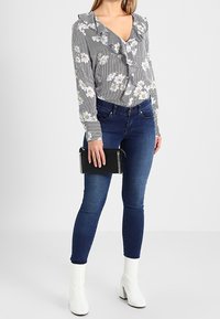 Vita anklar stövlar, mörkblå slim fit jeans och en långärmad svart och vit randig blus med blommiga detaljer och volangkrage.