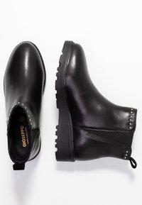 Botas de tobillo de cuero negro con un ligero tacón, superficie texturizada, paneles laterales elásticos y remaches plateados cerca del tobillo. Suela de goma con relieve.