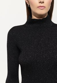 Schwarzes geripptes Rollkragenoberteil mit einer strukturierten, glitzernden Oberfläche und enganliegender Silhouette. Besitzt einen hohen Kragen und lange Ärmel.