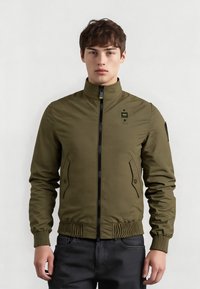 Giacca bomber verde oliva con colletto alto, chiusura frontale con zip, tasche laterali e polsini a costine; realizzata in un tessuto morbido e leggero.