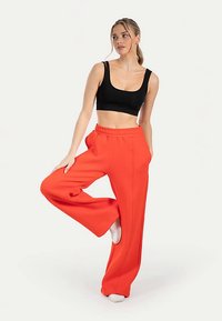 Zwart cropped top met dunne bandjes, gecombineerd met losse, hooggesneden rode broek met een ontspannen pasvorm en een elastische tailleband.