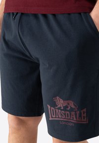 Tamsiai mėlyni medvilniniai šortai su elastinga juosta, su burgundiško raudonumo liūto logotipu ir u�žrašu "LONSDALE LONDON" kairėje šlaunyje.