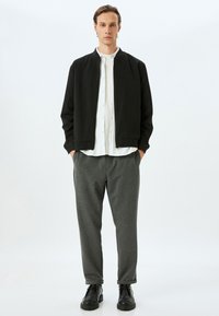 Sort bomberjakke, hvid skjorte med knapper, grå bukser. Glat stof, afslappet pasform og minimalistisk design. Sorte sko fuldender outfittet.
