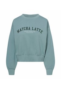 Jasnoniebieski skrócony sweatshirt z miękkiego materiału. Posiada okrągły dekolt, długie rękawy oraz wyraźny napis "MATCHA LATTE" w ciemnozielonym kolorze.