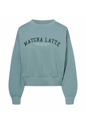 Jasnoniebieski skrócony sweatshirt z miękkiego materiału. Posiada okrągły dekolt, długie rękawy oraz wyraźny napis "MATCHA LATTE" w ciemnozielonym kolorze.