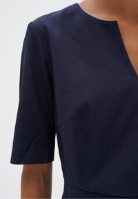 Mörkblå klänning med rund halsringning och korta ärmar. Slätt tyg med en subtil lyster. Inkluderar en liten fickdetalj fram.