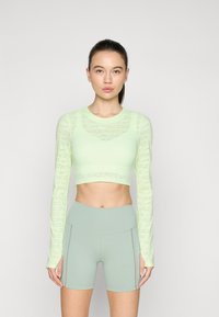 Jasnozielony krótki crop top z długim rękawem o subtelnej wzorzystej fakturze, w połączeniu z dopasowanymi szortami o wysokim stanie z bocznymi akcentami.