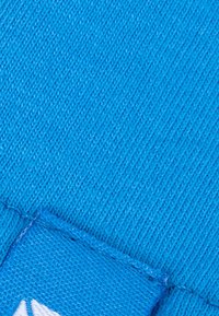 Helles blaues Gewebe mit strukturierter Oberfläche, das eine sichtbare Naht und ein Etikett mit einem weißen Logo am Rand hat.