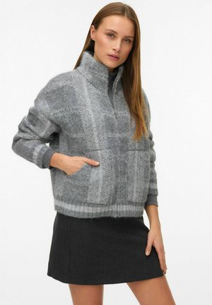 Veste pull en mélange de laine grise avec un col haut, un ourlet côtelé et deux poches avant, présentant un motif de tricot texturé et une coupe décontractée.