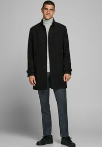 Melns mētelis ar pogu priekšpusi un sānu kabatām, uzvilkts virs gaiši pelēka roll-krekla. Saskaņots ar pelēku svītrainu biksēm un melniem sporta apaviem.