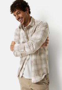 Beiges Flanellhemd mit blauem und braunem Karomuster, langen Ärmeln, Knopfleiste vorne und leichtem Material, kombiniert mit einem weißen T-Shirt.