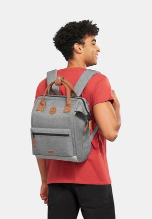 Sac à dos gris avec des accents en cuir marron, poignées supérieures, bretelles réglables et une poche zippée à l'avant. Tissu texturé avec un surpiquage sur les côtés.