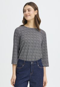 Langærmet top i navyblå med hvidt blomsterprint; rund halsudskæring og blødt stof. Kombineret med mørkeblå denimbukser.