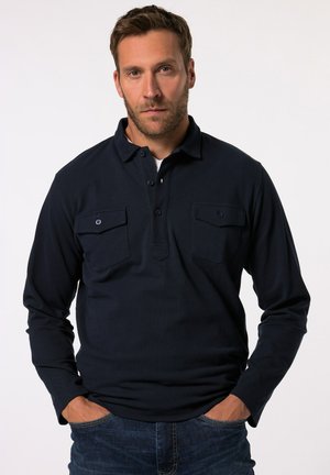 Polo de manga larga color navy hecho de un tejido texturizado que presenta dos bolsillos frontales con solapas de botón, acompañado de unos jeans azul.