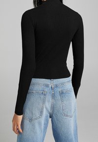 Haut noir côtelé à manches longues avec col montant, coupe ajustée et tissu texturé, associé à un jean en denim bleu clair taille haute.