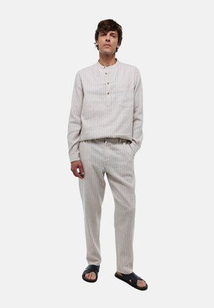 Tenue rayée de couleur claire en tissu, composée d'une chemise à manches longues avec des boutons sur le devant et un pantalon assorti, accompagnée de sandales noires.