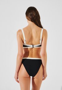 Fekete bikini strukturált anyagból, fehér részletekkel és állítható vállpántokkal. Hátul kapcsos rögzítéssel rendelkezik.