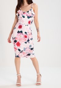Vestido midi floral con silueta ajustada. Presenta flores rosas y verde oscuro sobre un fondo claro, tirantes con volantes y una textura de tela suave.
