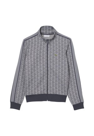 Grijze ritssluiting jas met geometrisch patroon, donkere boorden en zoom, strepen langs de mouwen en klein groen krokodillenlogo op de borst.