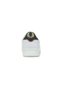 Sneaker bianco in pelle con un tallone nero, caratterizzato da un emblema dorato di alloro e dettagli rossi. Suola texturizzata e design minimale.