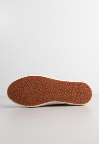 Gummisulor med en strukturerad yta och ljusbrun färg. Vita sidodetaljer och en ren design utan synlig märkning.