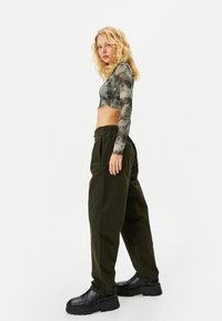Långärmad tie-dye croptop i grön och grå, ihop med mörkgröna cargobyxor med elastisk midja. Svarta chunky klackstövlar fulländar looken.