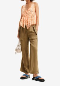 Haut orange à motifs avec ourlet à volants, associé à un pantalon cargo ample olive avec poches. Sandales noires avec accents bleus et petit sac.