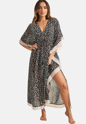 Kaftan noir transparent avec un motif de girafe blanc, décolleté en V, taille cintrée et bordure blanche contrastante, avec une fente haute sur la cuisse.