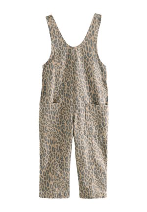 Junges Mädchen in Overalls mit Leopardenmuster, weißem Langarmshirt, rosa Strickmütze und rosa Sneakers steht neben einem großen orangen Ball und einem geometrischen Hintergrund.