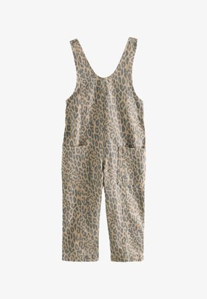 Junges Mädchen in Overalls mit Leopardenmuster, weißem Langarmshirt, rosa Strickmütze und rosa Sneakers steht neben einem großen orangen Ball und einem geometrischen Hintergrund.