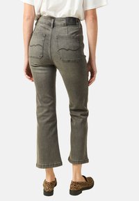 Szare jeansy z denimu o wysokim stanie i zwężających się nogawkach, z zaokrąglonymi tylnymi kieszeniami i surowym wykończeniem. W połączeniu z butami typu slip-on w panterkę.