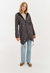 Melnbalta pārbauda jaka ar krāsainām sirds rakstiem, kapuci un aukliņu. Pāris ar gaiši ziliem džinsiem un rakstainām apaviem.