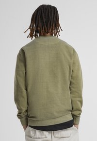 Olivgrön sweatshirt med en texturerad finish, rund halsringning och ribbad mudd. Har en avslappnad passform och rak fåll.