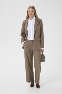 Brun skræddersyet jakkesæt med en enkelt-knaps blazer, bukser med vide ben, hvid skjorte under og en lille brun håndtaske. Glat stoftekstur.