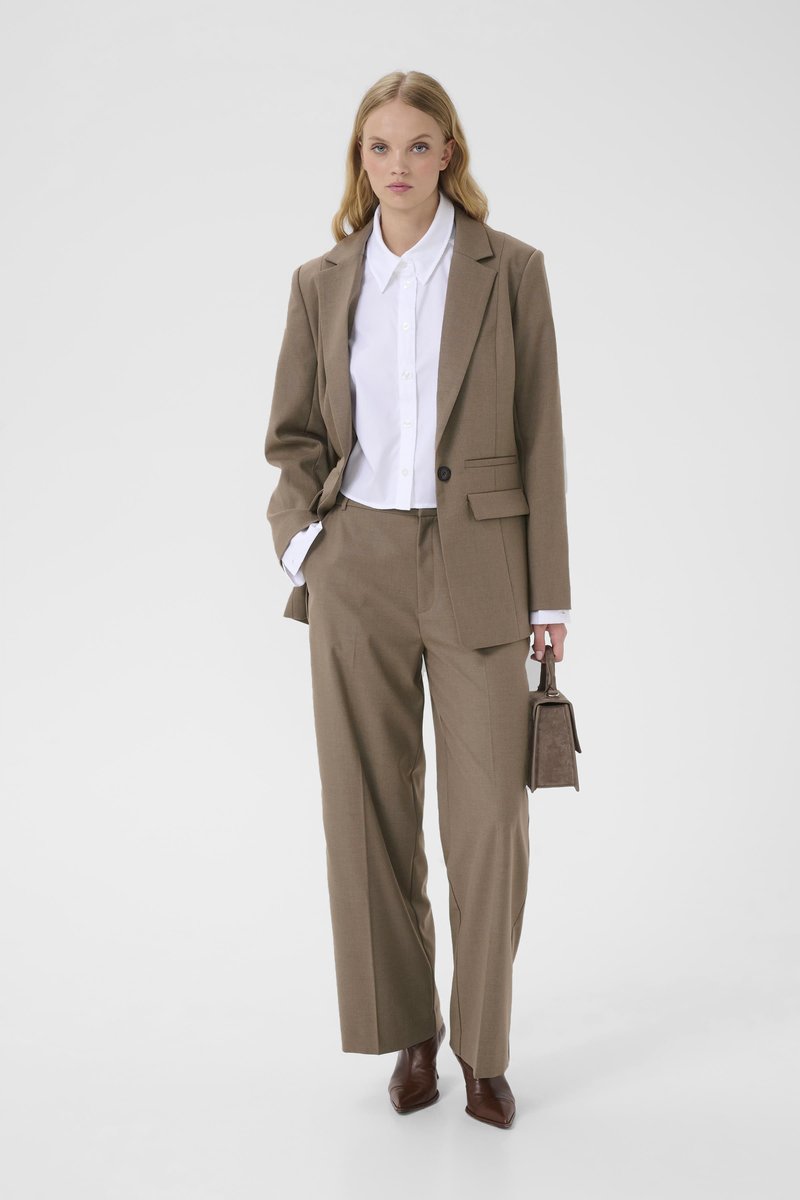 Costume marron sur mesure avec une veste à un bouton, pantalon à jambes larges, chemise blanche en dessous et un petit sac à main marron. Texture de tissu lisse.