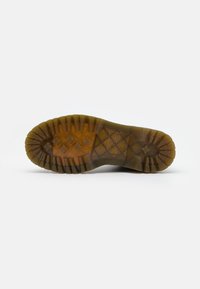 Semelle de botte en caoutchouc, marron avec des motifs de bande de roulement profonds. Présente une couche transparente sur une surface texturée avec une subtile empreinte de logo.