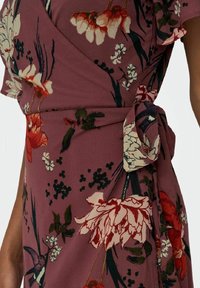 Vestido envolvente de tela color malva con patrones florales en rojo, blanco y verde. Incluye mangas cortas con volantes y un lazo en la cintura.
