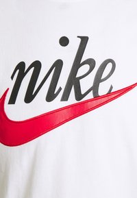 Biała bawełniana koszulka z krótkim rękawem z napisem "nike" w kolorze czarnym oraz logo czerwonego swooshu. Gładka faktura, casualowy design.