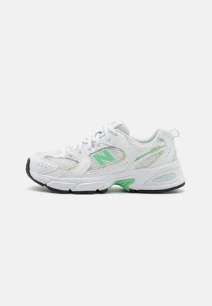 Hvid og grøn New Balance sportssko med mesh-paneler, snørebånd og sort gummisål vist fra siden på hvid baggrund.