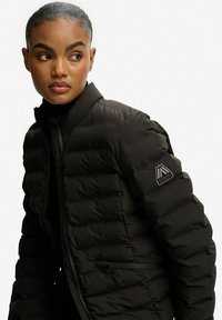 Czarna kurtka puchowa z wysokim kołnierzem, z pikowanym wzorem i naszywką z logo na rękawie. Slim fit, z zapięciem na zamek i eleganckim designem.