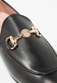 Černé kožené slip-on mokasíny se zlatou dekorativní sponou s logem a hladkým povrchem na svršku.