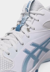 Λεπτομερής εικόνα ενός λευκού και γαλάζιου αθλητικού παπουτσιού Asics που δείχνει τα κορδόνια, το υφαντό ύφασμα και τις λεπτομέρειες του λογότυπου στο πλάι και στη γλώσσα.