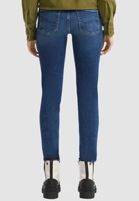 Jeans de mezclilla azul ajustados con un acabado texturizado, cinco bolsillos y costuras en contraste. Usados con botines negros y blancos.