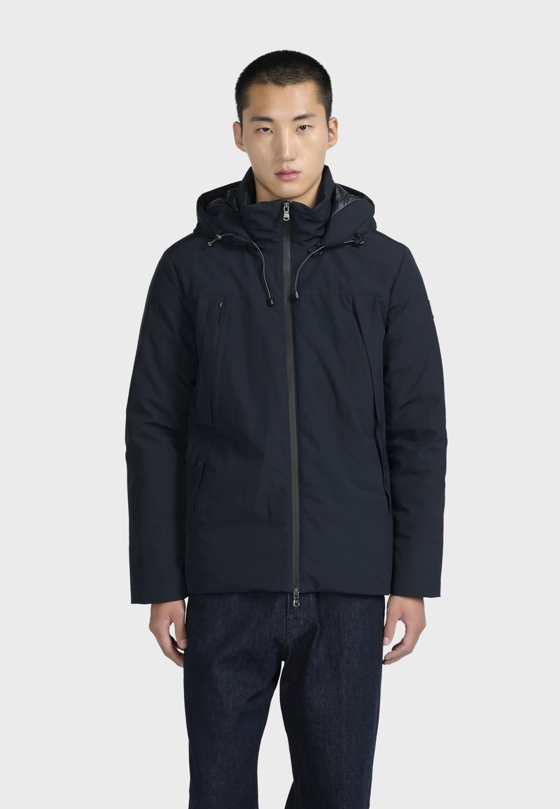 Tmavě modrá zateplená bunda s kapucí, předním zipem a nastavitelnými šňůrkami. Obsahuje kapsy na zip po bocích. Textura látky se zdá být hladká.