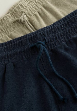 Two pairs of drawstring sweatpants: one in light olive green, the other in navy blue. Both feature ribbed waistbands and soft textures.