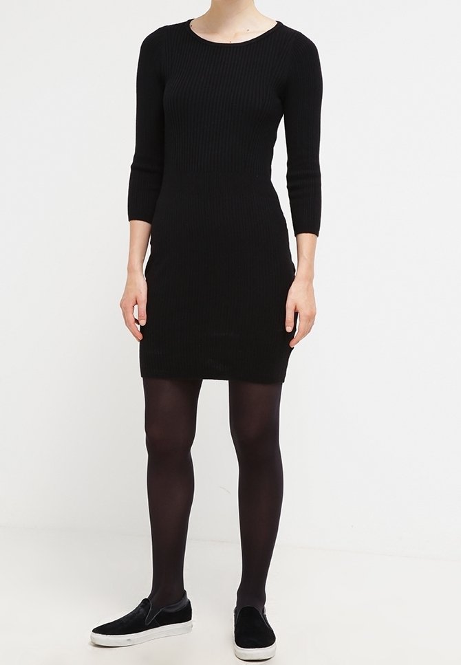 Svart ribbad klänning med trekvartslånga ärmar, åtsittande form och rund halsringning, kombinerad med svarta strumpbyxor och svarta slip-on sneakers.