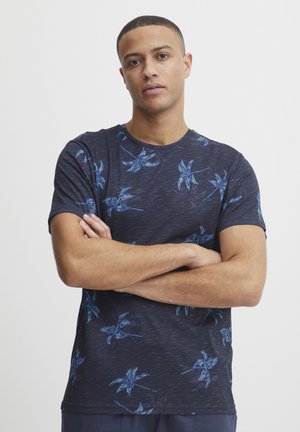 Marineblå t-shirt med korte ærmer, lavet af blødt stof med en diskret tekstur; har et blåt palmebladsmønster over forsiden.